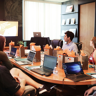 A meeting room with a long table, laptops open, and gift bags placed around, as participants engage in discussion.